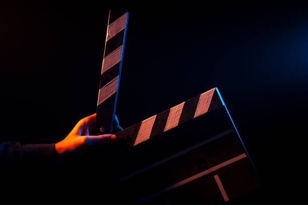 バックライトを赤と青と黒の孤立した背景に撮影の前に、手で映画館のカチンコを開く - projectionist ストックフォトと画像