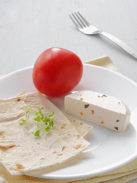 Mediterranean breakfast served on white plate. Soft cheese with vegetables and cress salad with fresh pita bread. Vertical. Selective focus on the center. stock photo