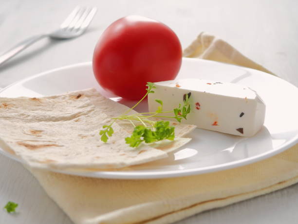 Piece of cheese with vegetables and grocery served with fresh pita bread on white plate. Healthy breakfast. stock photo