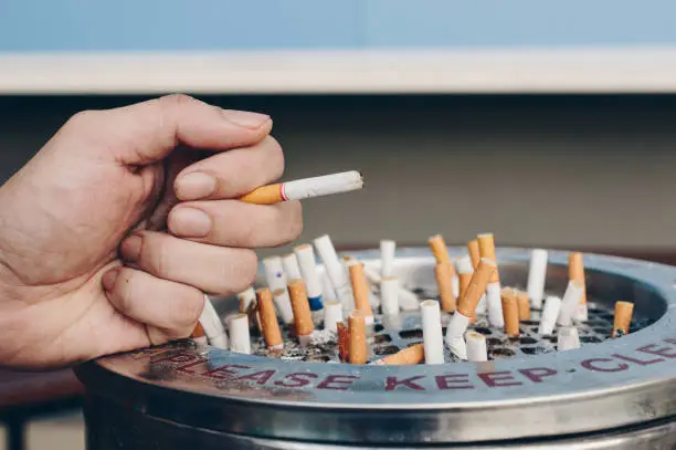 Photo of Close-up of the hand of young man with group of Cigarettes left in the metal ashtray.