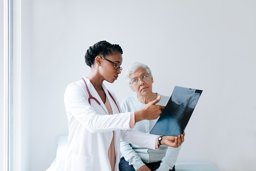 A young black female doctor showing an x-ray to a senior female patient and explaining.