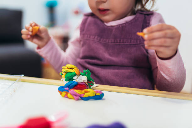 istock Kid girl is playing with plasticine while sitting at table in nursery room 1065314758