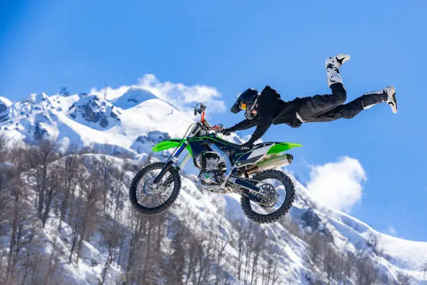 racer on a motorcycle in flight, jumps and takes off on a springboard against the snowy mountains. Concept active extreme rest. ray of light