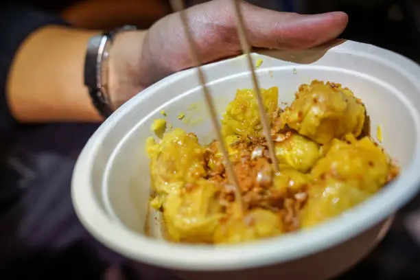 A yellow steamed dumpling topping with fried garlic put in the paper cup. At Bangkok Thailand foodstruck streetfood.