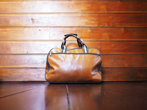 Close up old brown leather bag with handle on wooden floor in vintage room.