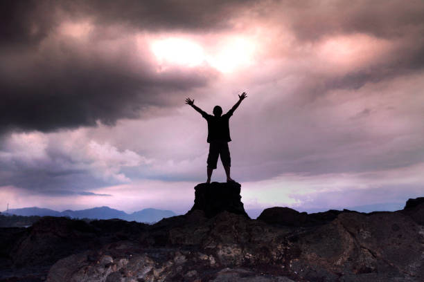 istock a man on the rock raises his  hand up in cloudy storm 1065323546