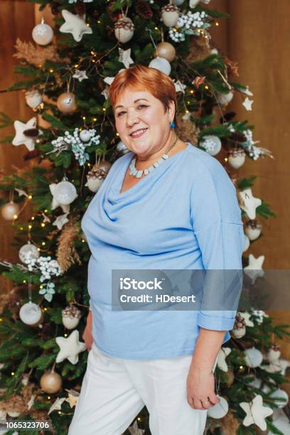 Smiling Senior Woman Posing Near Christmas Tree Stock Photo - Download Image Now - Adult, Adults Only, Christmas