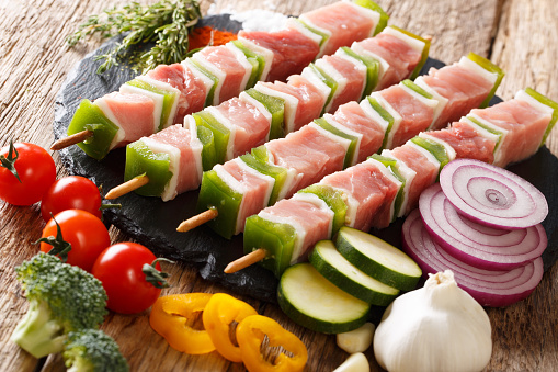 Preparation of barbecue: raw shish kebab with green pepper on skewers close-up and vegetables, herbs on the table. horizontal