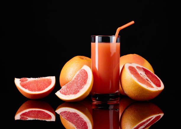 Glass of  grapefruit juice and cut fruits on black background.