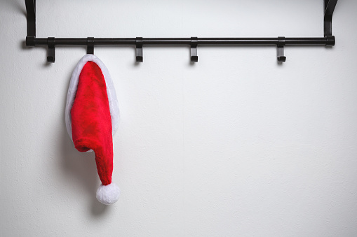 Minimalistic shot of a red Santa hat on a cloak hanger on a white wall.