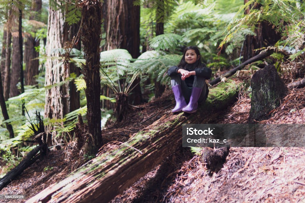 Girl sitting on a fallen tree trunk A candid photograph of a 9-year old eurasian girl sitting on a fallen tree trunk in the Redwood Forest, Rotorua New Zealand Stock Photo