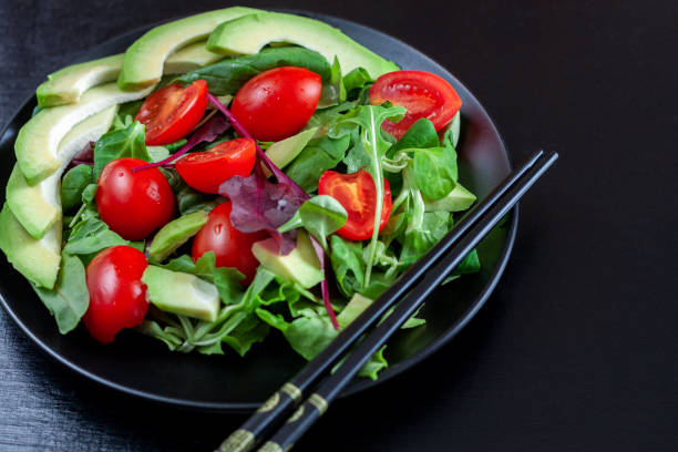 istock Vegetable salad with avocado, cherry tomatoes, arugula and spinach on a black plate on a dark background. 1065377360