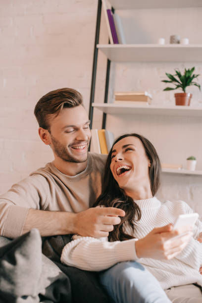 istock laughing young couple using smartphone together on couch at home 1065392034