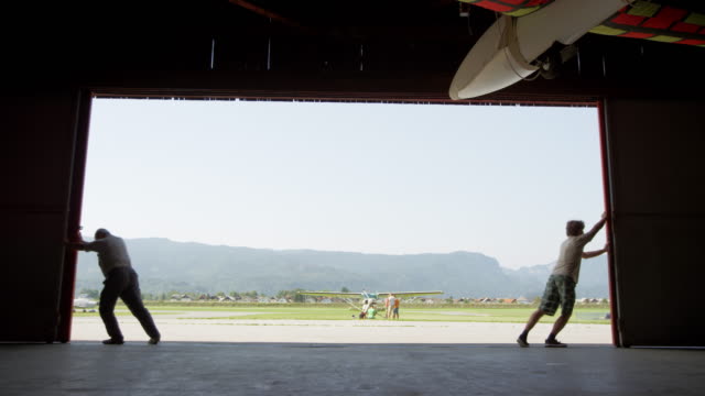 Two men opening the door of the hangar at the airport and revealing a sunny airport