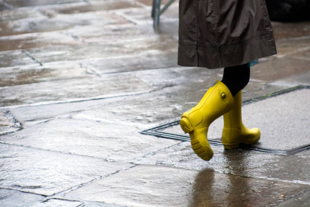 caminhando no chão de pedra de pavimentação rua molhada usando chuva amarela botas... - human leg women shower water - fotografias e filmes do acervo