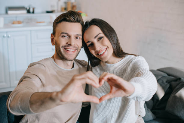istock beautiful young couple making heart symbol with hands and looking at camera 1065395638