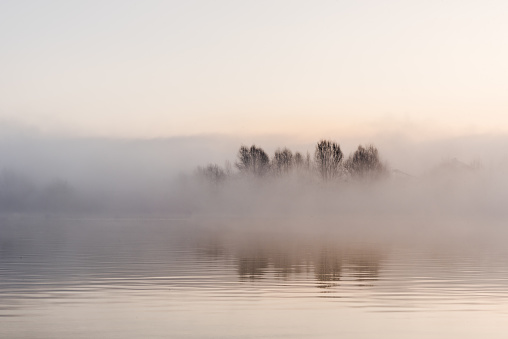 Family paddles canoe on tranquil lake at sunrise on a misty morning