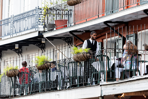 New Orleans, USA - April 22, 2018: Old town Bourbon Decatur street in Louisiana town, city, cast iron balcony building, waiter, people sitting in restaurant