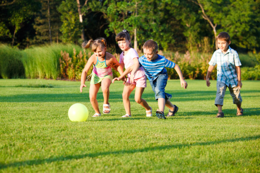 Diverse children playing soccer outdoors on summer, happy boys and girls kicking football ball. Kids leisure activity, entertainment in nature, wide shot