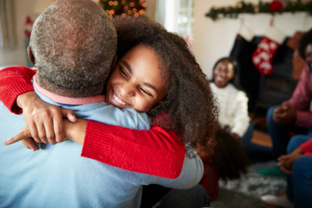Granddaughter Giving Grandfather Hug As Multi Generation Family Celebrate Christmas At Home Granddaughter Giving Grandfather Hug As Multi Generation Family Celebrate Christmas At Home multi generation family christmas stock pictures, royalty-free photos & images