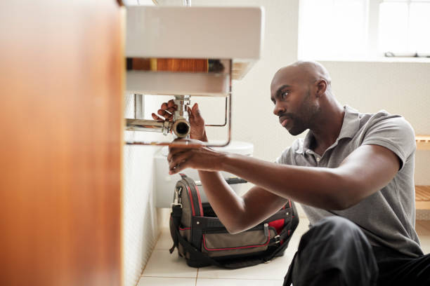 Young black male plumber sitting on the floor fixing a bathroom sink, seen from doorway Young black male plumber sitting on the floor fixing a bathroom sink, seen from doorway plumbing fixture stock pictures, royalty-free photos & images