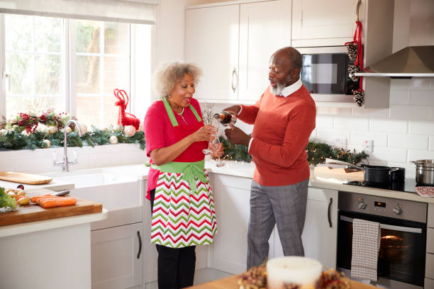 istock Senior black man pouring champagne for his partner in the kitchen while preparing dinner on Christmas Day, selective focus 1065441024