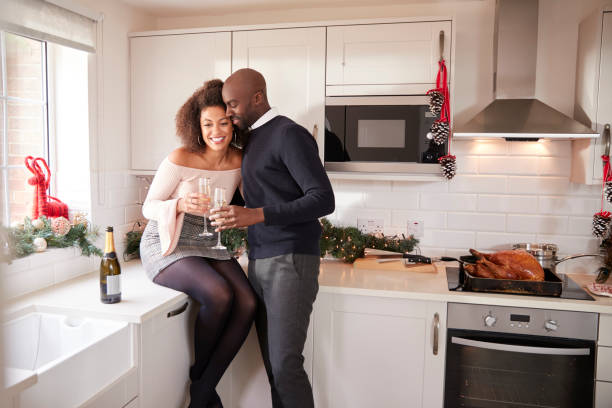 istock Young mixed race couple drinking champagne embrace in their kitchen while preparing Christmas dinner 1065443608