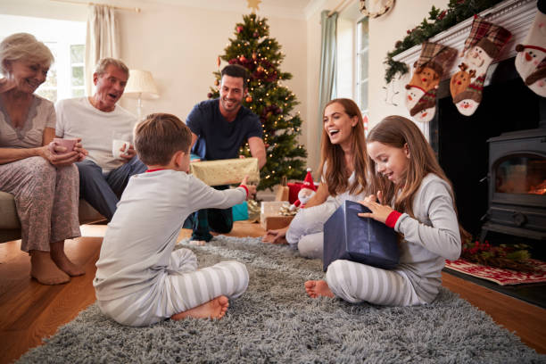 drei-generationen-familie tragenden pyjamas lounge im hause öffnung geschenke am ersten weihnachtstag - opening present stock-fotos und bilder