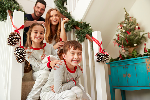 Portrait Of Excited Family Wearing Pajamas Sitting On Stairs On Christmas Morning