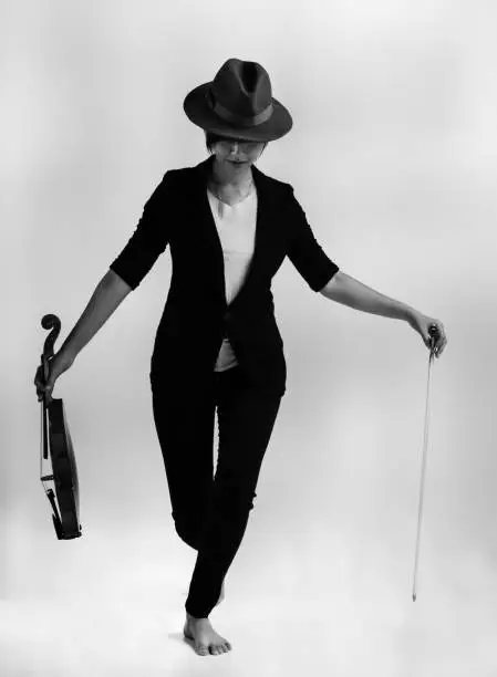 The lady is wearing black suit and brown hat,stand on stage and hold violin and bow in hand,prepare for playing,art tone