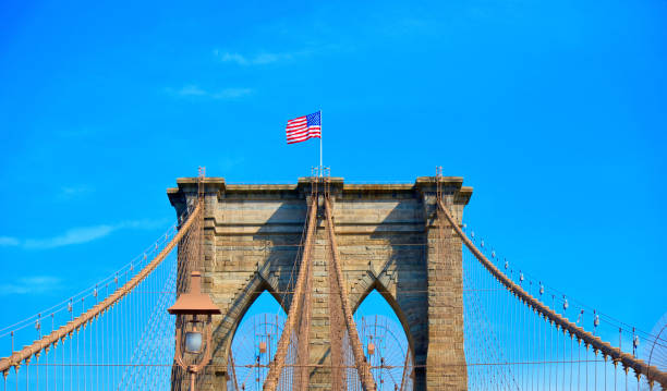 istock iconic brooklyn bridge construction with american flag, arch and modern patterns against blue sky in Manhattan, Ney York 1065467382