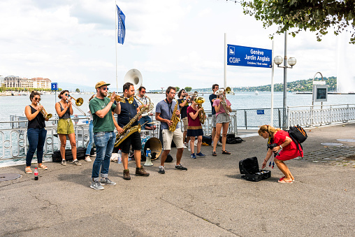Geneva, Switzerland - August 24, 2018: Street musicians in Lake shore at Geneva, Switzerland. They are playing classic or jazz music with some instrument and earning money by using classic musical instruments (violin, cello, tuba, saxophone, trumpet, trombone, drum, etc) in sidewalk of Geneva. Tourist woman is giving money.