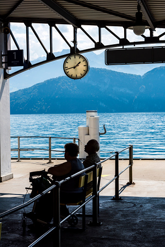 Weggis, Switzerland - August 22, 2018: Two adult passengers are waiting for the ferry to arrive in Weggis port. Bikes and motorcycles parked on the side in port.