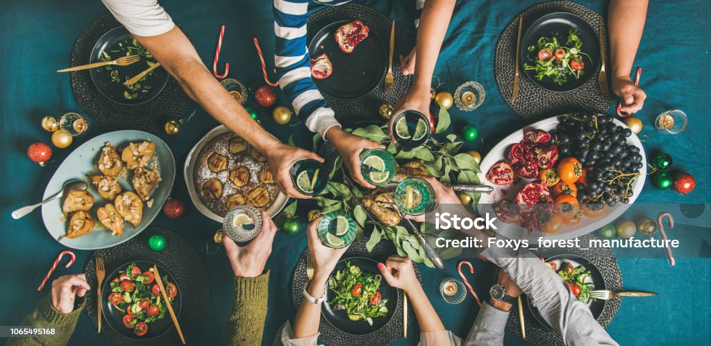 Company of friends or family gathering for Christmas dinner Company of friends of different ages or family gathering for Christmas or New Year party dinner at festive table. Flat-lay of human hands holding glasses with drinks, feasting and celebrating holiday together, top view. Christmas Stock Photo