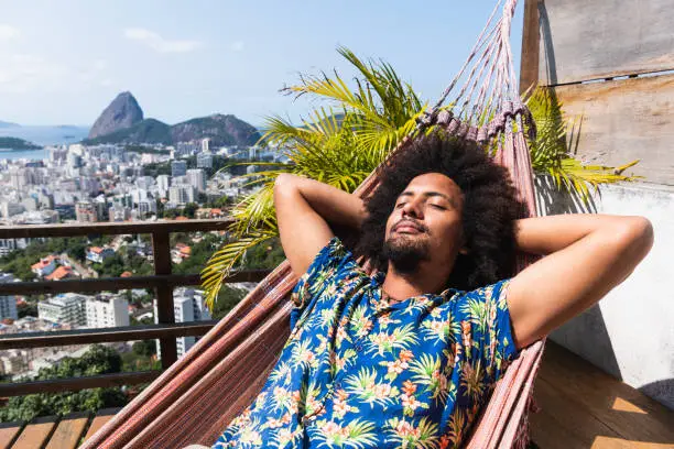 Young man sleeping in Hawaiian shirt, relaxing on balcony, sunbathing in Rio de Janeiro