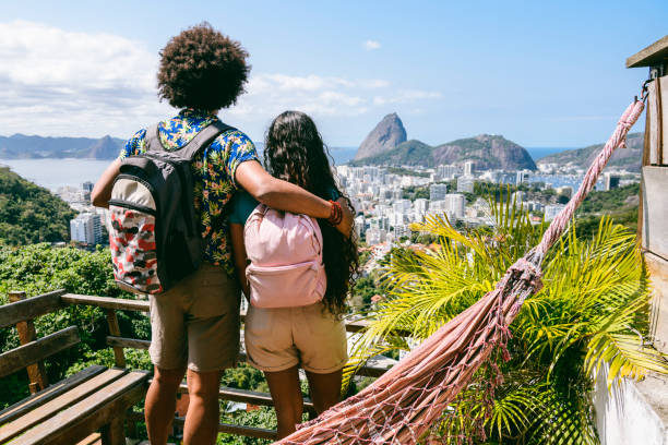 Rear view of two backpackers looking at view of Sugar Loaf Mountain Man and woman wearing backpacks, looking at city scape, elevated view from balcony, on vacation casa stock pictures, royalty-free photos & images