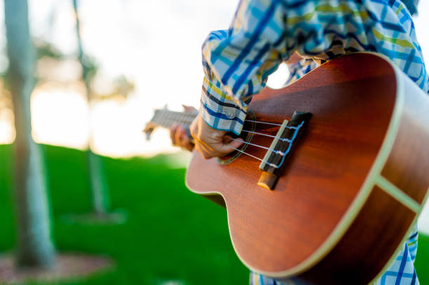 closeup of hand of young child playing acoustic guitar in park outdoor at sunset stock photo