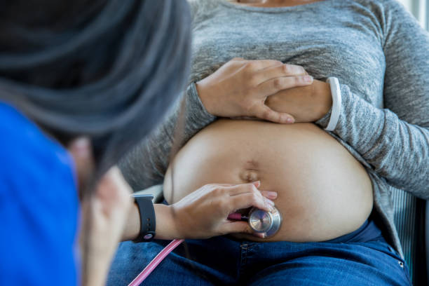 Pregnant African American mid adult patient being examined with a stethoscope Mid adult pregnant African American patient being examined with a stethoscope.  Prenatal exam with and Asian female nurse, midwife or doctor. midwife photos stock pictures, royalty-free photos & images