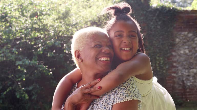 Senior black woman and granddaughter sit embracing outside