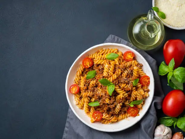 Bolognese pasta. Fusilli with tomato sauce, ground minced beef, basil leaves. Traditional italian cuisine. Top view, copy space