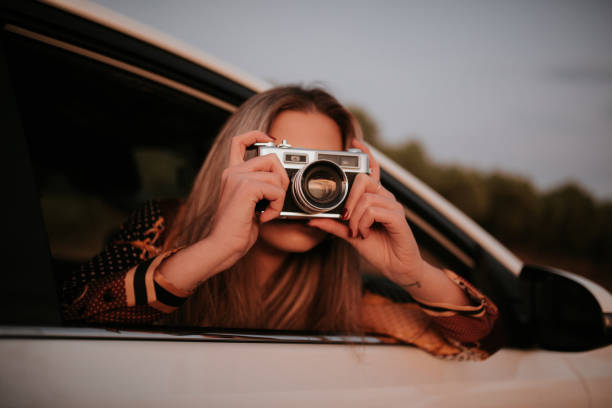 Young woman taking a picture with a vintage camera from car window stock photo