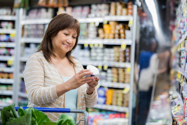 Senior adult Asian female is shopping at a grocery store Senior adult Asian female is shopping at a grocery store. She is reading nutrition facts on the label. She has brown hair and is shopping alone. nutrition label stock pictures, royalty-free photos & images