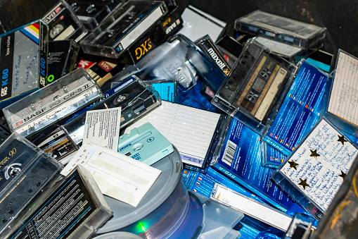 Berlin, Germany - October 23, 2018: View of many discarded old radio play and music cassettes, CDs and DVDs in a garbage bin.