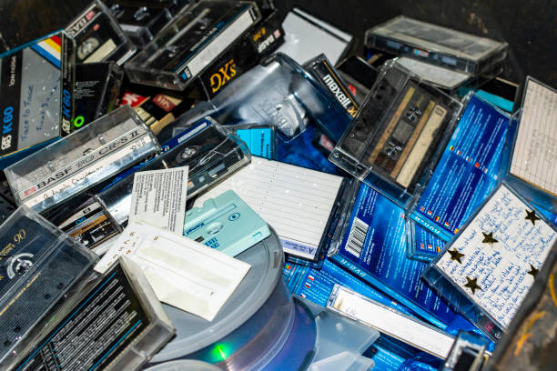 view of many discarded old radio play and music cassettes, cds and dvds in a garbage bin. - dvd stack cd movie imagens e fotografias de stock