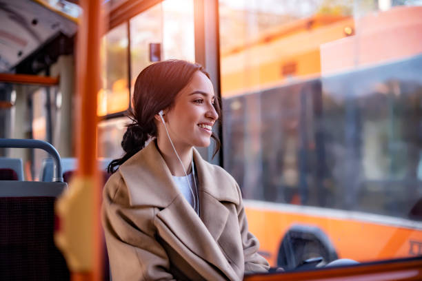 Tunes to travel by One Young Woman Smiling in a Bus While Listening to Music using Earphones. Beautiful Young Woman With Earphones Taking Bus to Work. The Passenger Listening to Music in the Bus or Train, Technology Lifestyle, Transportation and Traveling Concept. bus stock pictures, royalty-free photos & images