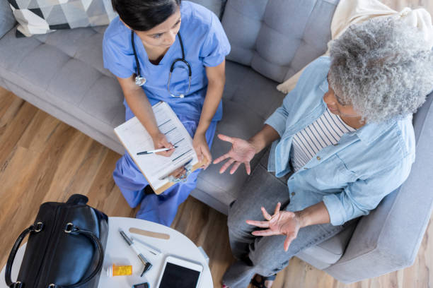 Bird's eye view of doctor and patient discussion during house call In this bird's eye view, a female doctor sits on a living room couch with a senior female patient.  She holds a clipboard as the patient gestures and speaks.  There is a doctor's bag and medical equipment on the coffee table. doctors bag stock pictures, royalty-free photos & images