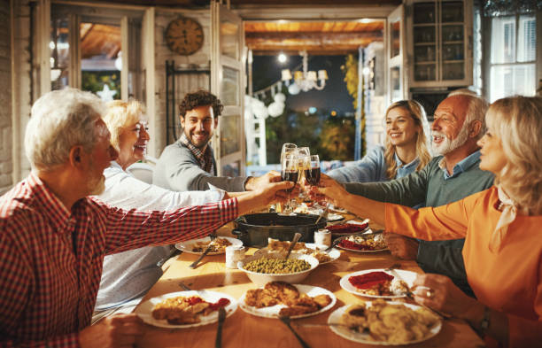Family having Thanksgiving dinner. Closeup side view of a family having a Thanksgiving or Christmas eve dinner. They are having a feast at a rustic vacation house while sipping some wine, talking and laughing. people banque stock pictures, royalty-free photos & images