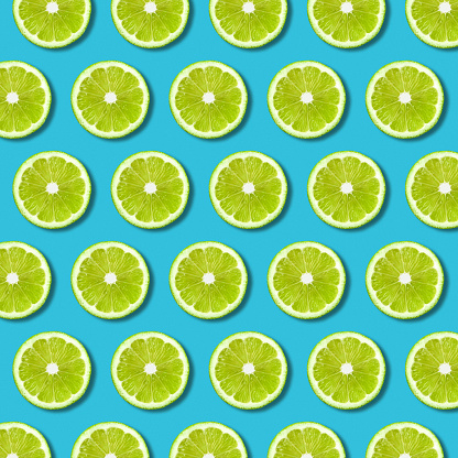 Green lime slices pattern on vibrant turquoise color background. Minimal flat lay food texture