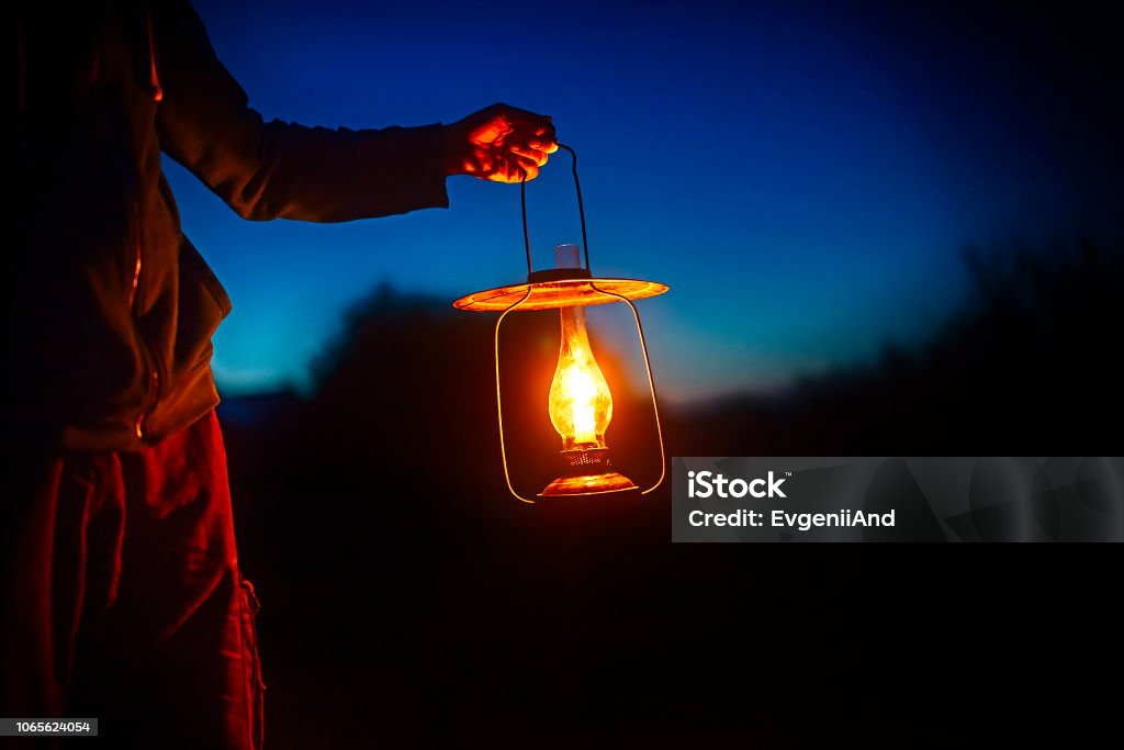 hand holds a large old lamp in the dark. man holding the vintage lamp with a candle outside. Copy space for your text Lantern Stock Photo