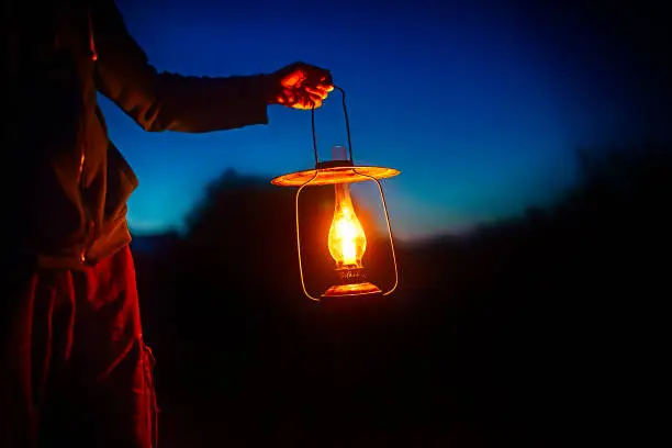 Photo of hand holds a large old lamp in the dark.